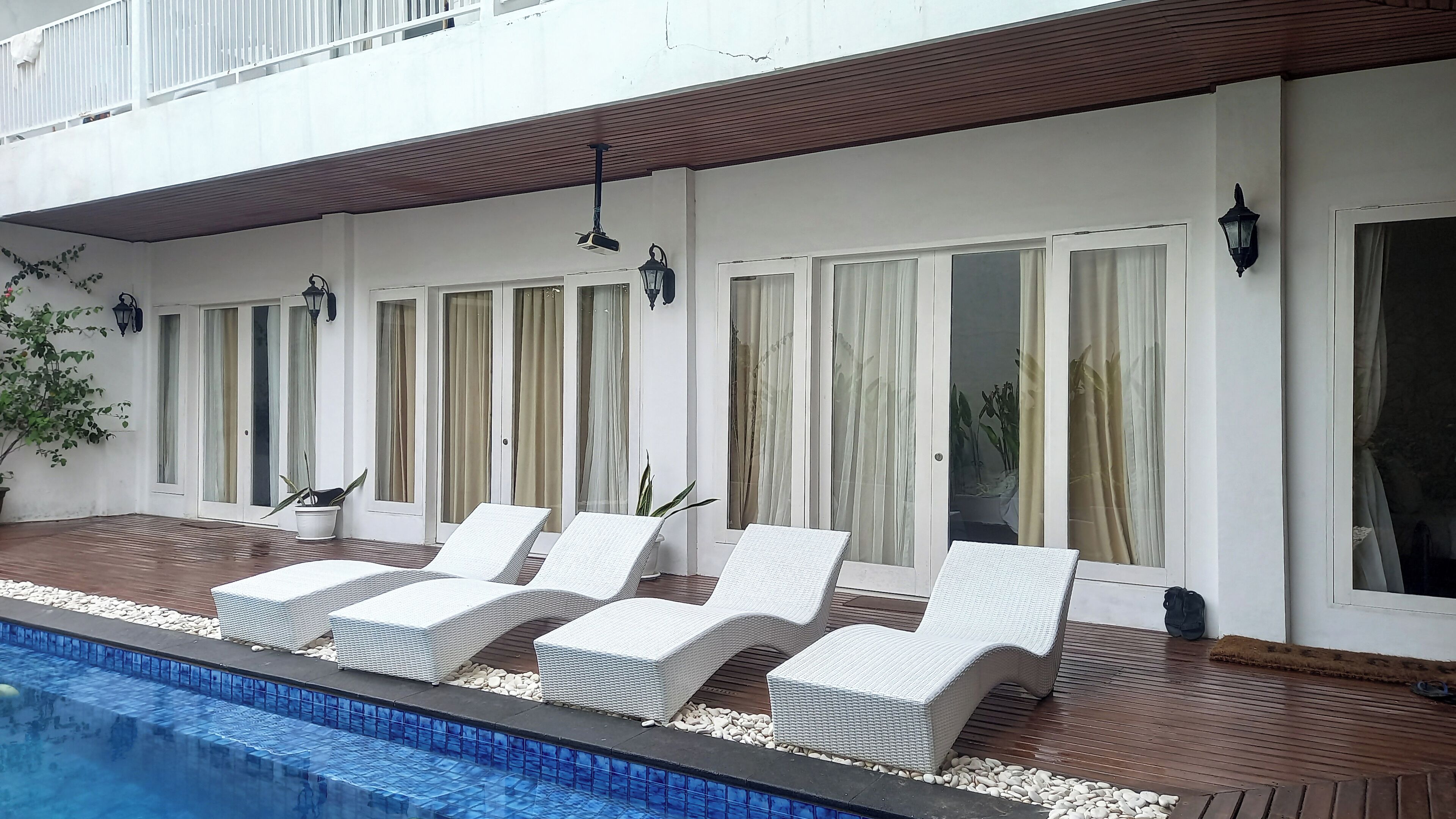 Zona junto a la piscina con sillones reclinables de mimbre blanco, una terraza de madera y una pileta.