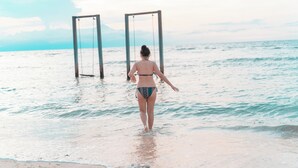 Una persona caminando hacia un columpio en la playa.