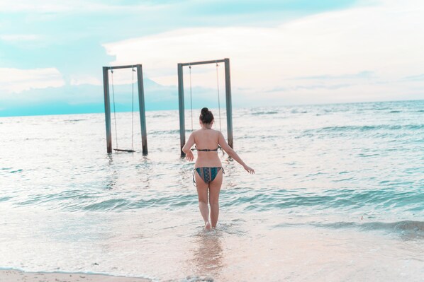 A person walking towards a swing set on a beach.