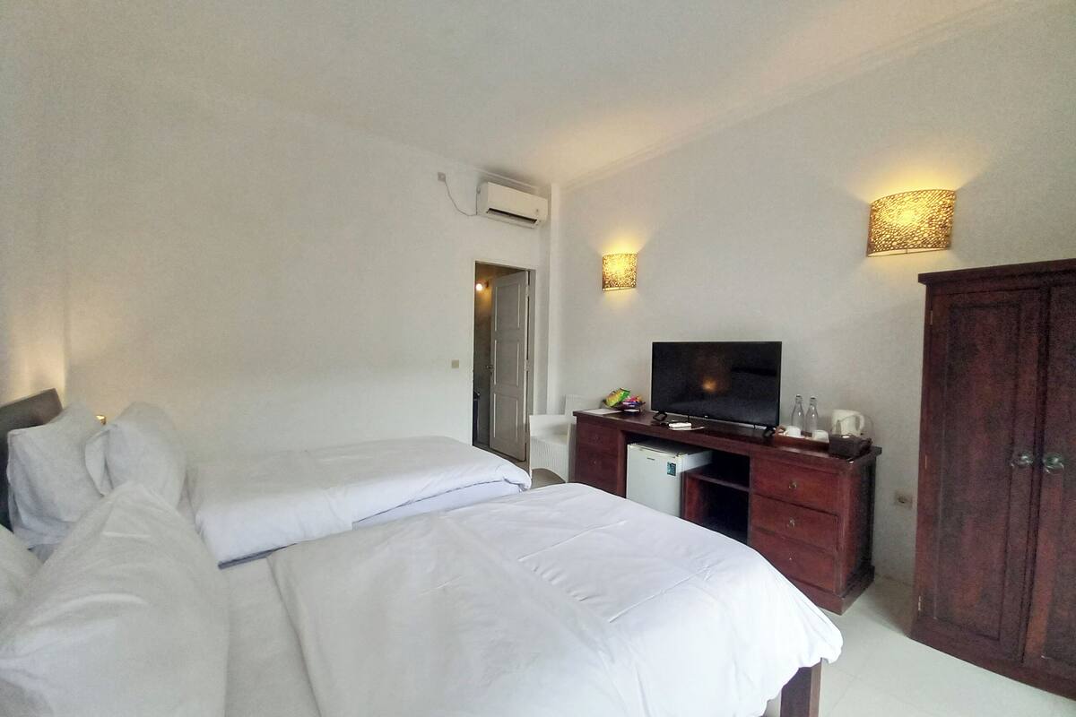 A hotel room with two beds, a TV, a minibar, and a wardrobe.