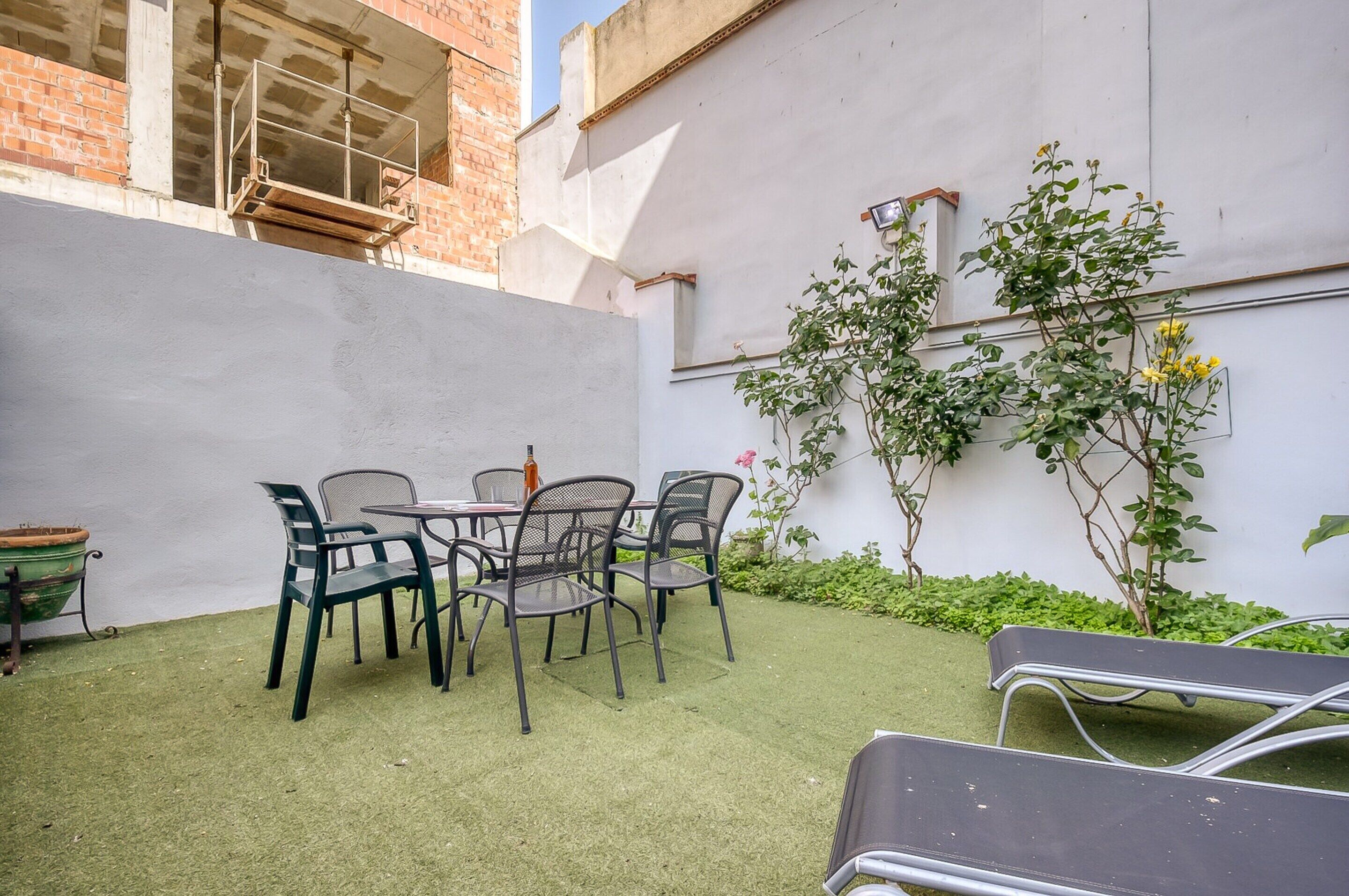 A patio area with a table and chairs, a potted plant, and a climbing plant against a wall.