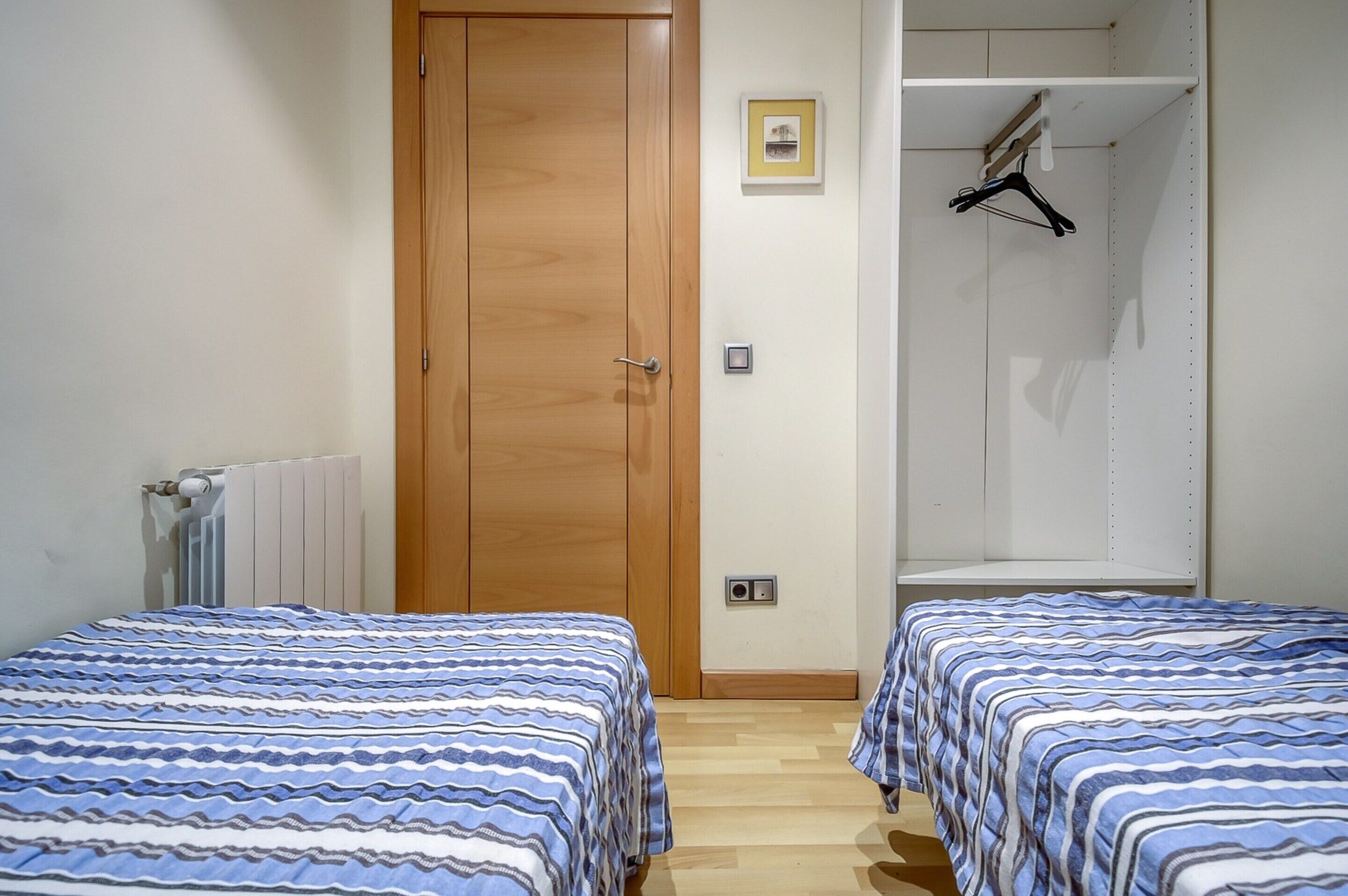 A bedroom with two beds, a wooden door, a radiator, a white wardrobe, and a framed picture on the wall.