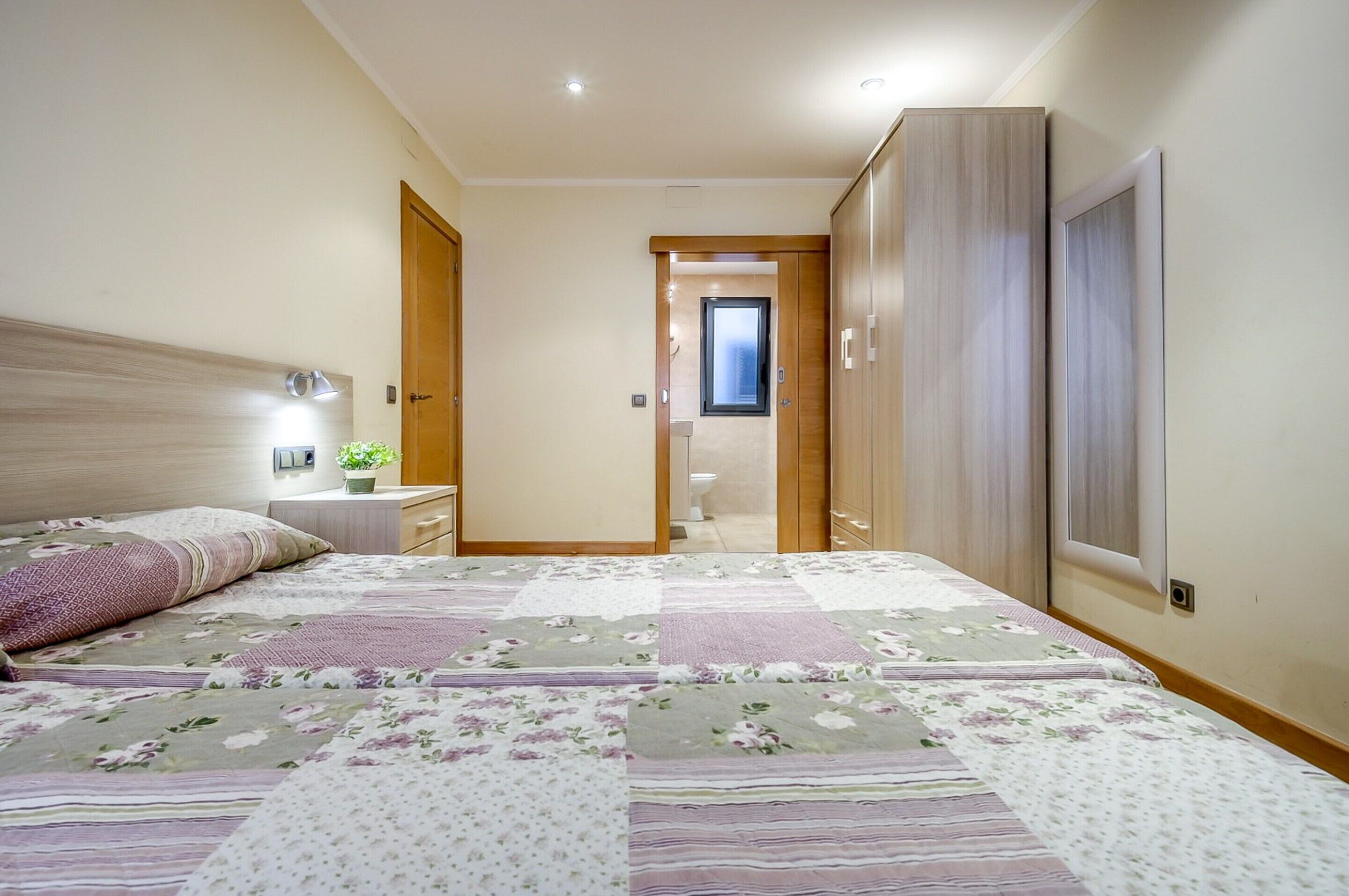 A bedroom with a large bed, a nightstand, a dresser, and a wardrobe.