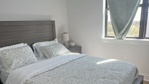 A bedroom with a large bed, a nightstand, a lamp, and a window with a view. - Cozy 1-bedroom apartment in Austin, centrally located in Mueller. (Austin)