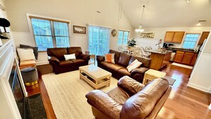 A spacious living room with leather sofas, a coffee table, and a kitchen area in the background.