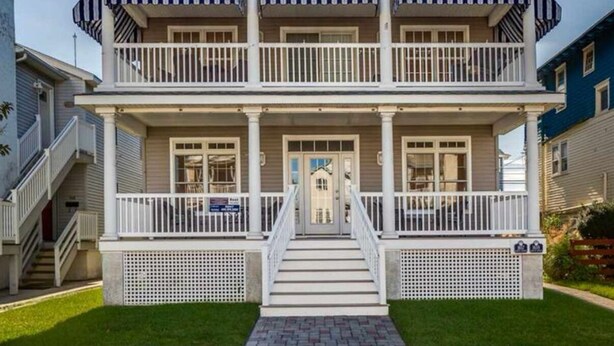 A two-story house with a front porch, a staircase leading to the entrance, and a circular window on the gable.