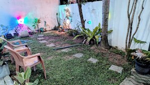 Un jardín con plantas en macetas, una silla de madera y un sendero de piedra.