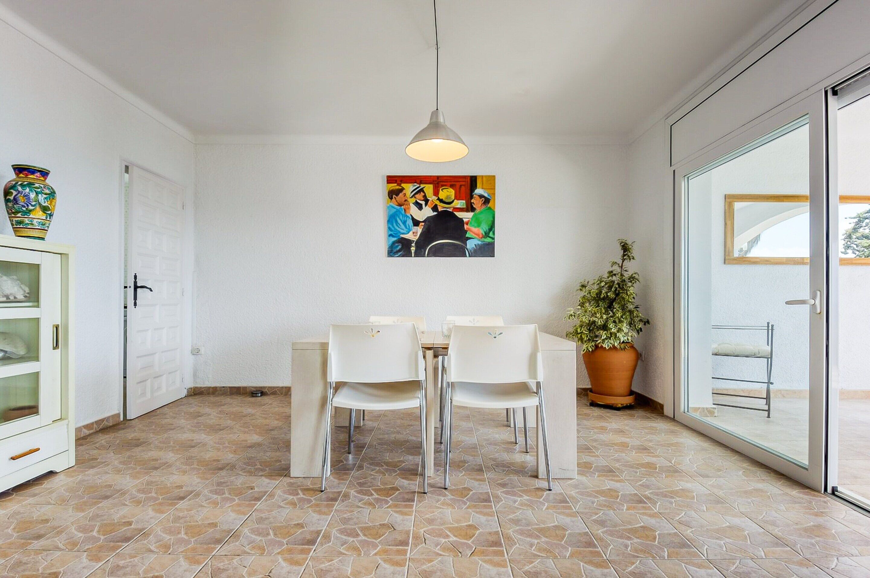 A dining area with a table and chairs, a hanging light fixture, a potted plant, and a painting on the wall.