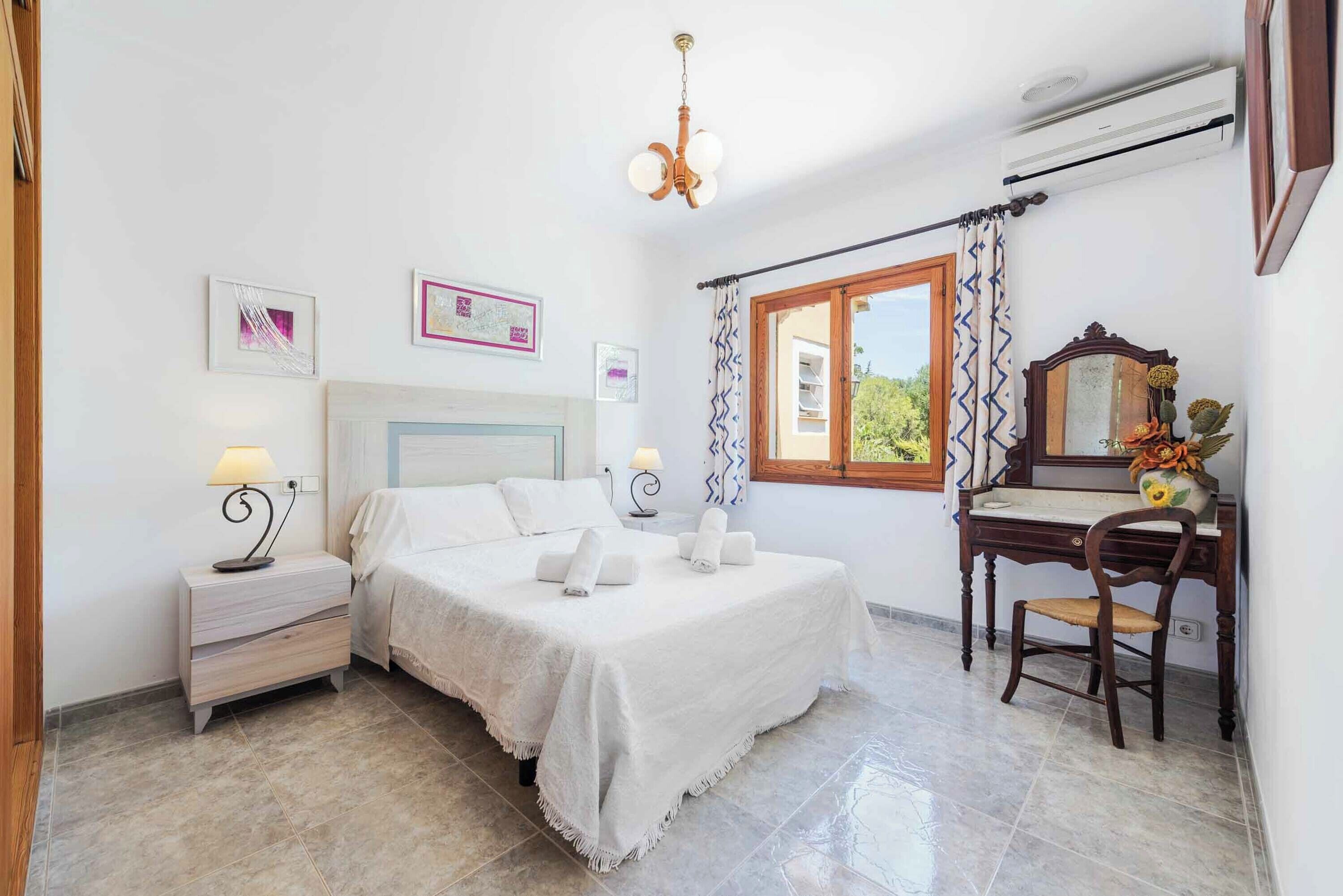 A bedroom with a bed, bedside table, lamp, and a desk with a chair.