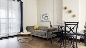 Un salon moderne avec un canapé gris, une table basse ronde et une table à manger avec des chaises.