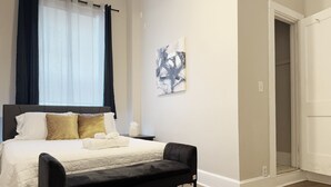 Une chambre à coucher bien rangée, avec un lit, une table de chevet, un banc et un tableau accroché au mur.