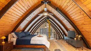 A bedroom with a sloped ceiling, a bed, a nightstand, a dresser, a television, and a window with a view. - Retro A-Frame w/ Hot Tub, Perfect Couple's Getaway (Island Park)