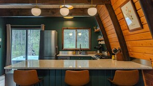 A kitchen with a large island, wooden walls, and a window overlooking a forest. - Retro A-Frame w/ Hot Tub, Perfect Couple's Getaway (Island Park)