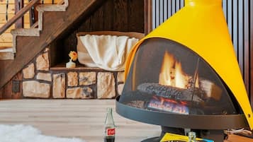 A cozy living room with a fireplace, a wooden staircase, and a dining area with a tray, dice, and a bottle of Coca-Cola.