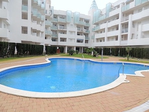 A swimming pool surrounded by a brick patio, with a multi-story building in the background. - Apartment in Roses Near Sand Beach (Roses)