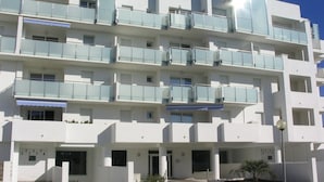 Un edificio moderno de varios pisos con balcones, una entrada cubierta y cielo despejado.
