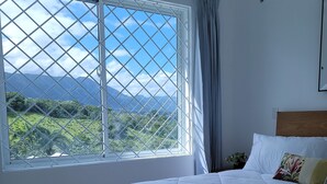 Un dormitorio con un ventanal grande, una cama con ropa de cama blanca y un cabecero de madera.