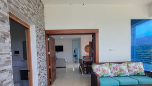 Un salón moderno con piso de madera, un sofá con cojines estampados y vista a un paisaje montañoso a través de un ventanal grande.