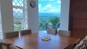 Un comedor con mesa y sillas de madera, ventanas amplias con vistas al exterior y una puerta.