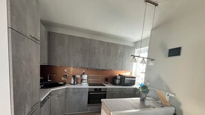 Una cocina compacta con armarios grises, horno empotrado, cafetera y refrigerador.