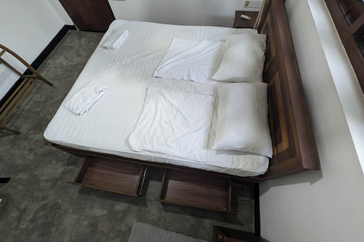 A neatly made bed with white linens and pillows, a wooden headboard, and a small bedside table with a lamp.