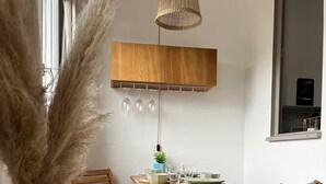A dining area with a wooden table, two chairs, a hanging light fixture, and a vase with dried plants. - The Pearl of the Cliffs (Le Tréport)