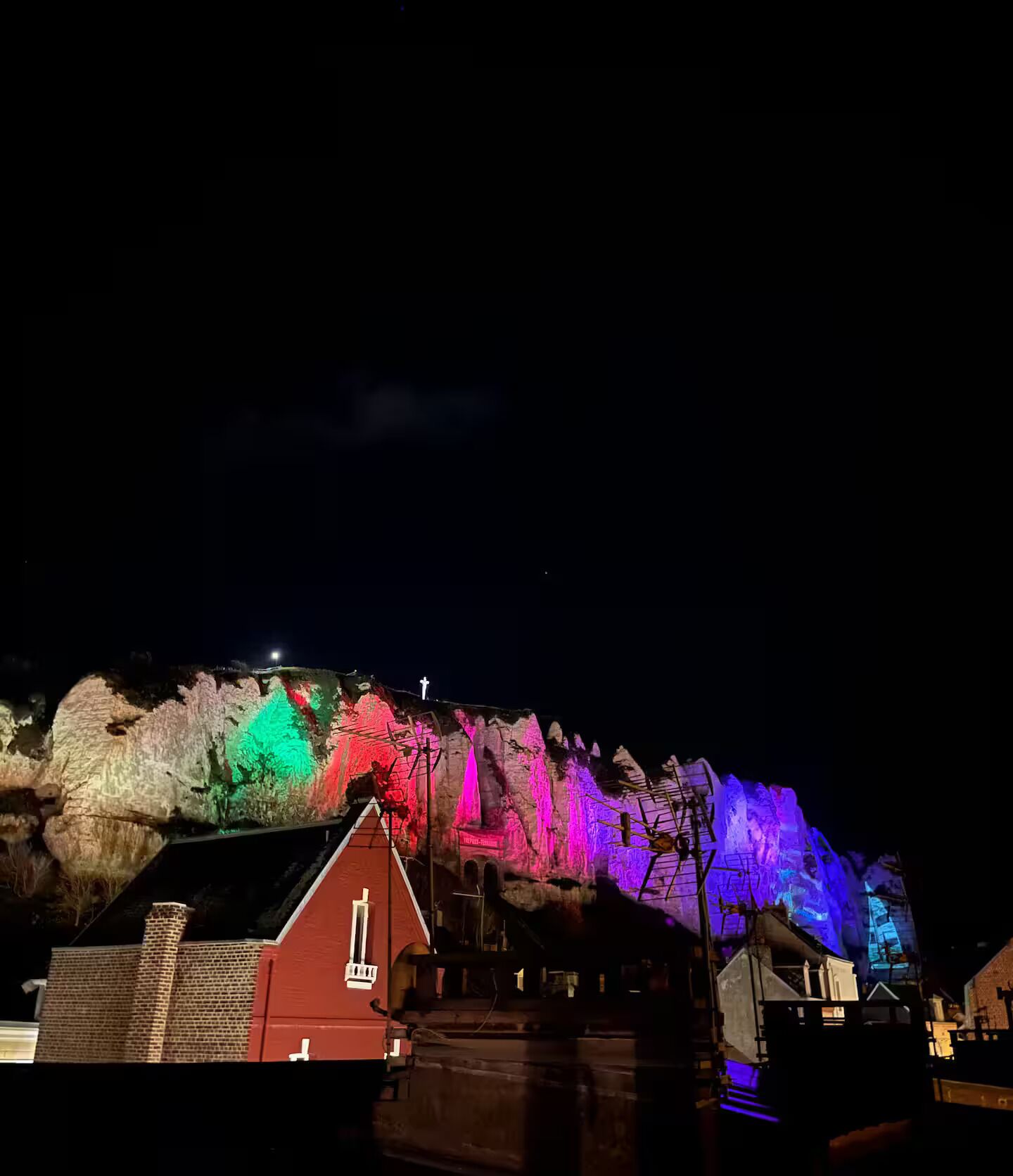 Een nachtzicht van een gebouw met een rood dak en een kruis bovenop, verlicht met kleurrijke lichten.