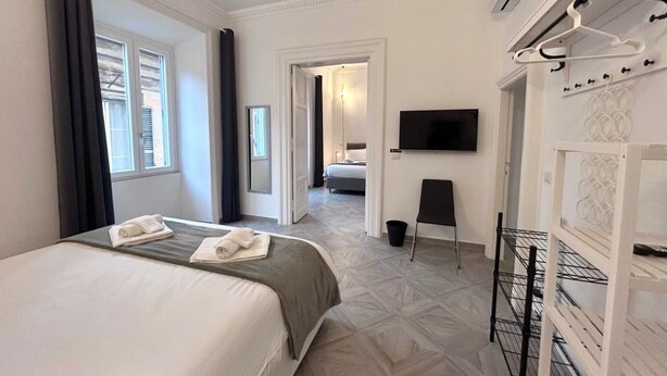A hotel room with a bed, a TV, a coat rack, and a hallway leading to another room. - Beautiful house in the heart of Rome 20meters from Piazza Venezia/Trevi Fountain (Roma)