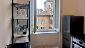 A kitchen with a window, a black refrigerator, and a metal shelf with glassware. - Beautiful house in the heart of Rome 20meters from Piazza Venezia/Trevi Fountain (Roma)