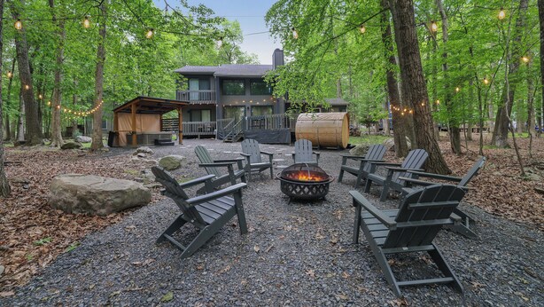 A rustic outdoor seating area with Adirondack chairs, a fire pit, and string lights.