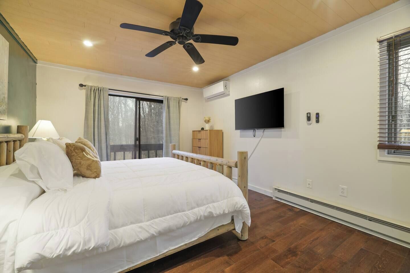 Une chambre à coucher avec un lit, un ventilateur de plafond, une télévision et une fenêtre avec des stores.