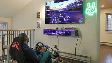 Iemand speelt een racegame op een televisiescherm, in een ruimte met een neonreclame en een gameconsole.