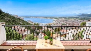 A balcony with a table, two wine glasses, and a bottle of champagne. The balcony overlooks a coastal city with a view of the sea and a hilly landscape. - Apartment in Rosas Near Cap de Creus (Roses)