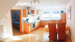 Une cuisine moderne avec des meubles en bois, un coin repas avec des chaises en osier et une vue sur la ville grâce à de grandes fenêtres.