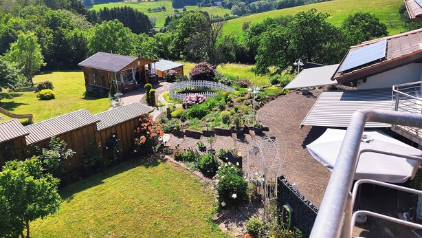 Un quartier résidentiel avec une maison dotée d’un jardin entouré d’une clôture en bois peinte en blanc, d’une allée pavée et d’un panneau solaire sur le toit.
