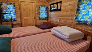 Una habitación de cabaña de madera con dos camas, una puerta de madera y una ventana con diseño de pez.