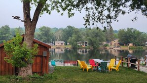 Una cabaña junto al lago con un muelle, un bote y sillas Adirondack de colores.