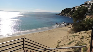 A coastal view with a sandy beach, a staircase leading down to the shore, and buildings on a hillside. - Apartment in Roses Near Sand Beach (Roses)