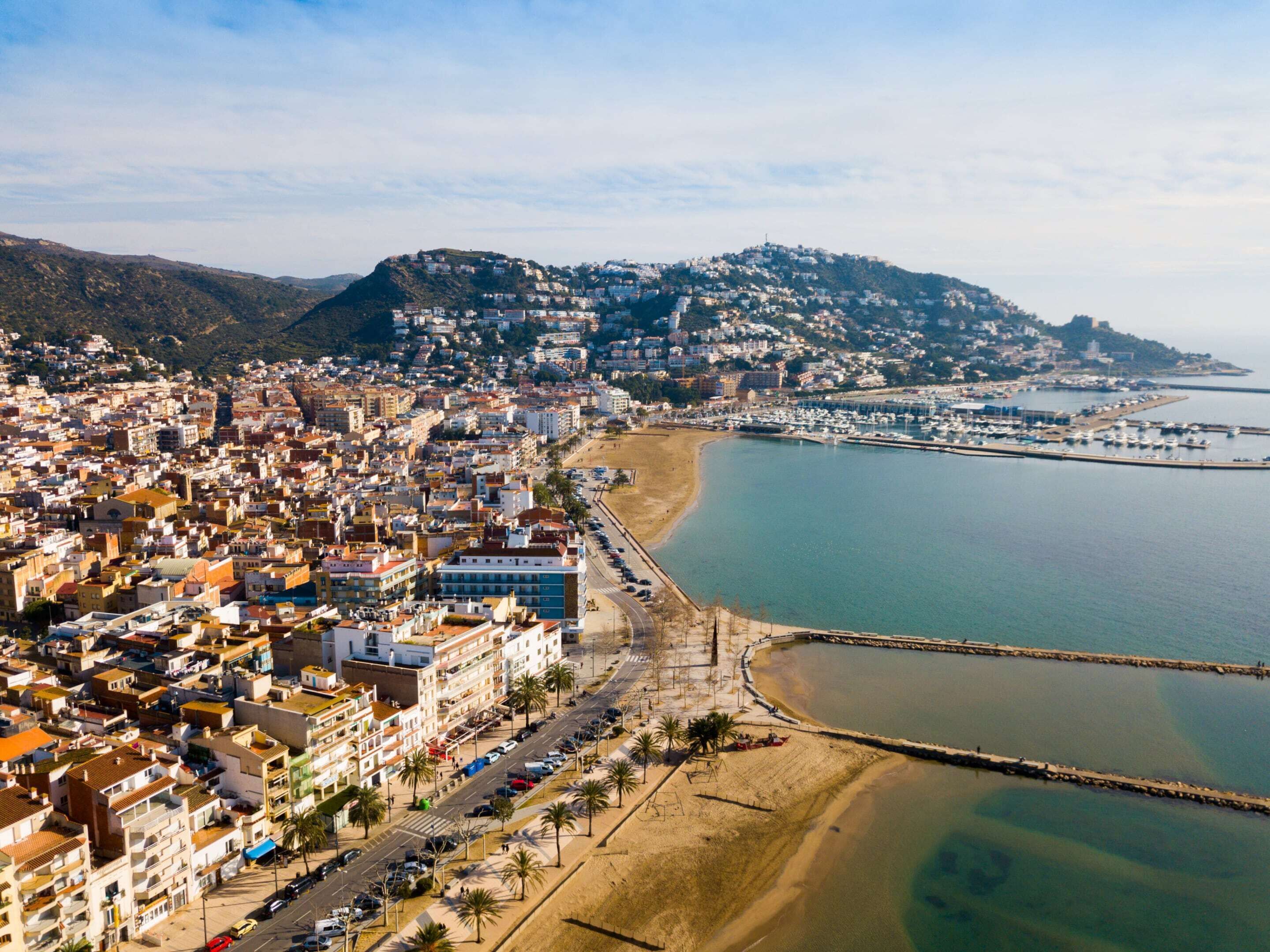 Vista aérea de una ciudad costera con un desarrollo urbano denso, un puerto deportivo y una playa.