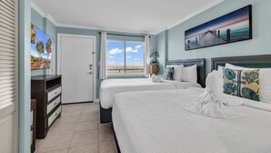 A hotel room with two beds, a large window with a view, a painting on the wall, and a desk with drawers. - Bluewater Resort 1205 (Myrtle Beach)