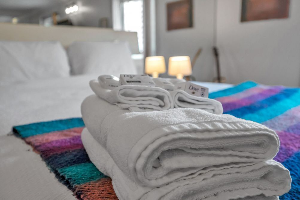 A neatly made bed with folded white towels and a colorful striped blanket.