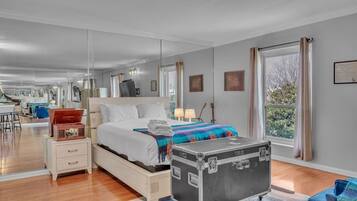 Una habitación de hotel moderna con una cama grande, lámparas de noche, una maleta y vistas al exterior.