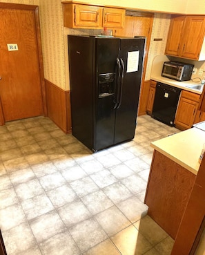 A compact kitchen with a black refrigerator, wooden cabinets, a microwave, and a dishwasher.