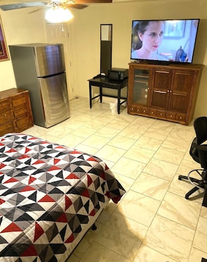A bedroom with a bed, a refrigerator, a television, a wooden cabinet, and a desk.