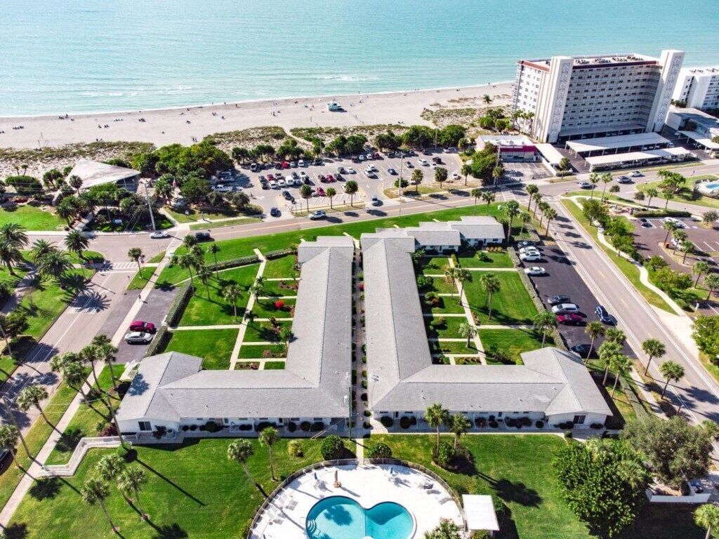 An aerial view of a hotel with a central courtyard, a pool, and a beach in the background.