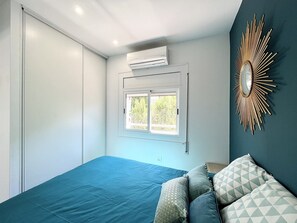 A bedroom with a bed, a window, an air conditioner, and a decorative mirror.