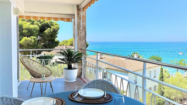A balcony with a table set for dining, overlooking a coastal view with the sea and boats. - Apartment Near Canyelles Petites Beach (Roses)