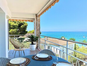 A balcony with a table set for dining, overlooking a coastal view with the sea and boats.