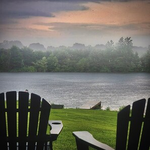 Une vue sur le lac, avec une pelouse et deux fauteuils Adirondack placés face à l’eau.