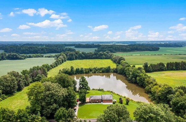 Ländliche Landschaft mit Teich, einem kleinen Gebäude und umliegender Bepflanzung.